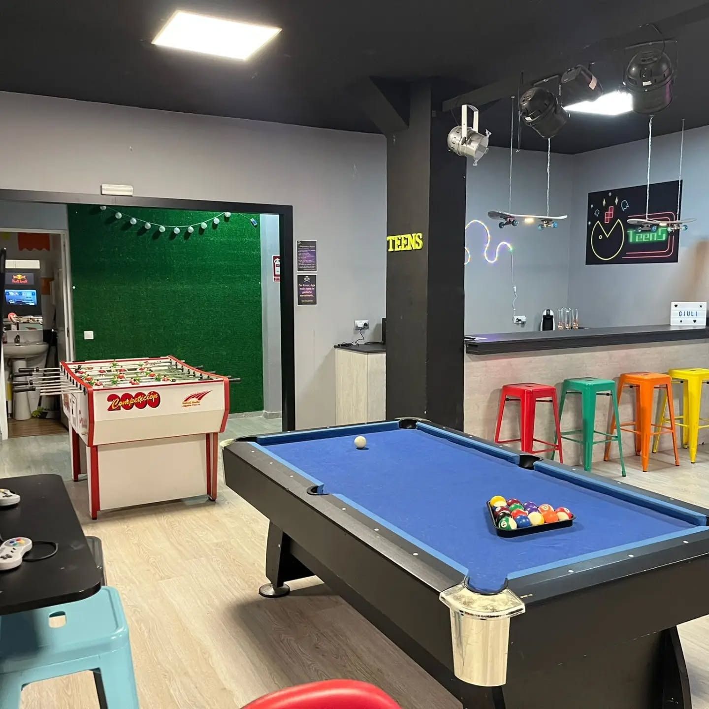 Mesa de billar, futbolín y barra con taburetes de colores