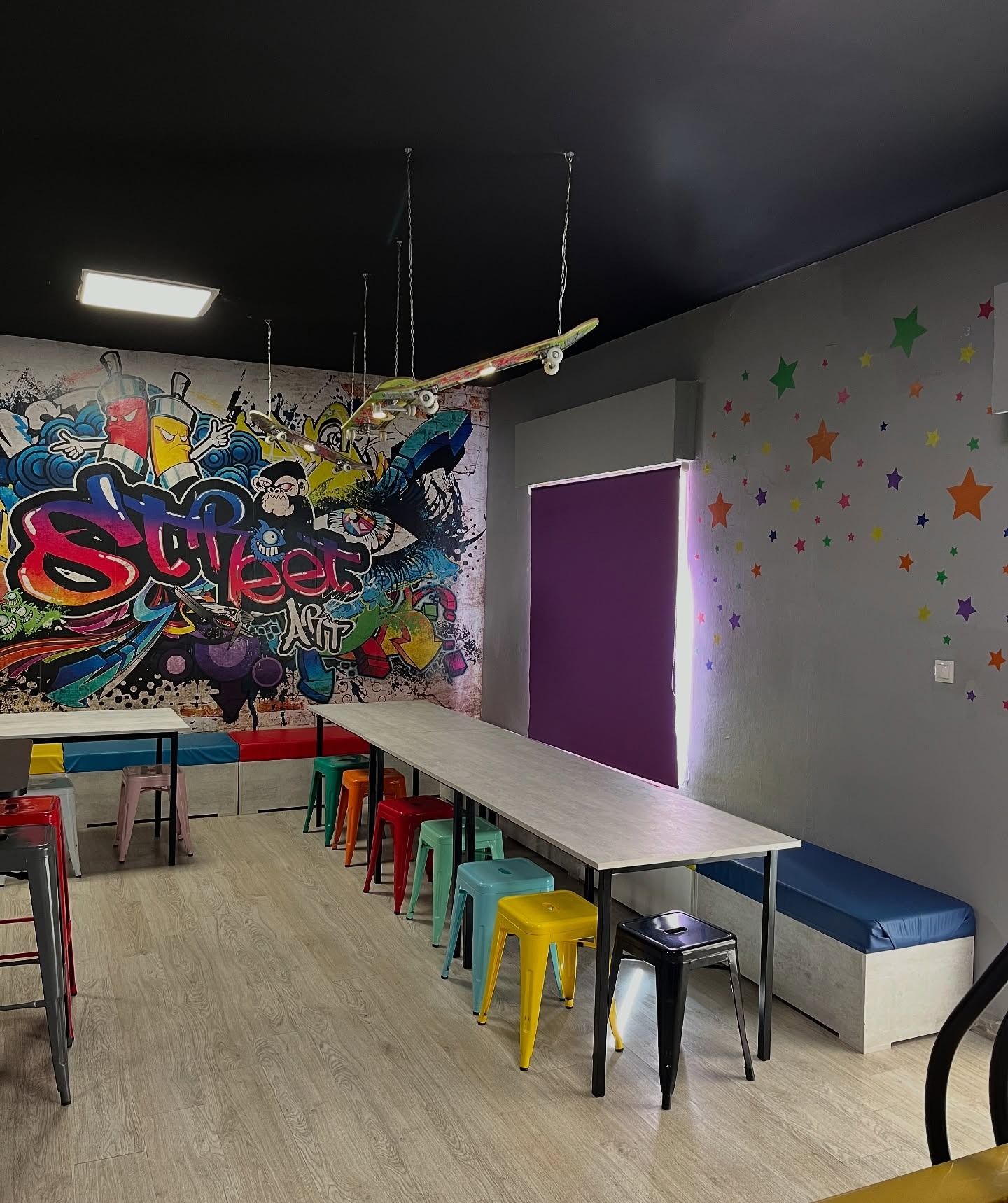 Zona para comer con mesas largas, taburetes de colores y mural de graffiti